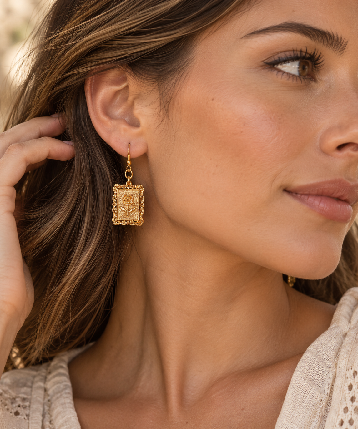 Modelo luciendo pendientes dorados ALMIREA de diseño rectangular con rosa en relieve y estilo elegante