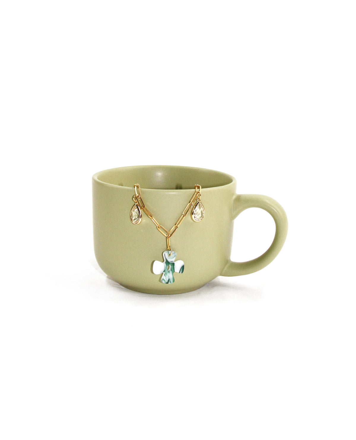 Collar Éden dorado con cruz verde presentado en fotografía decorativa